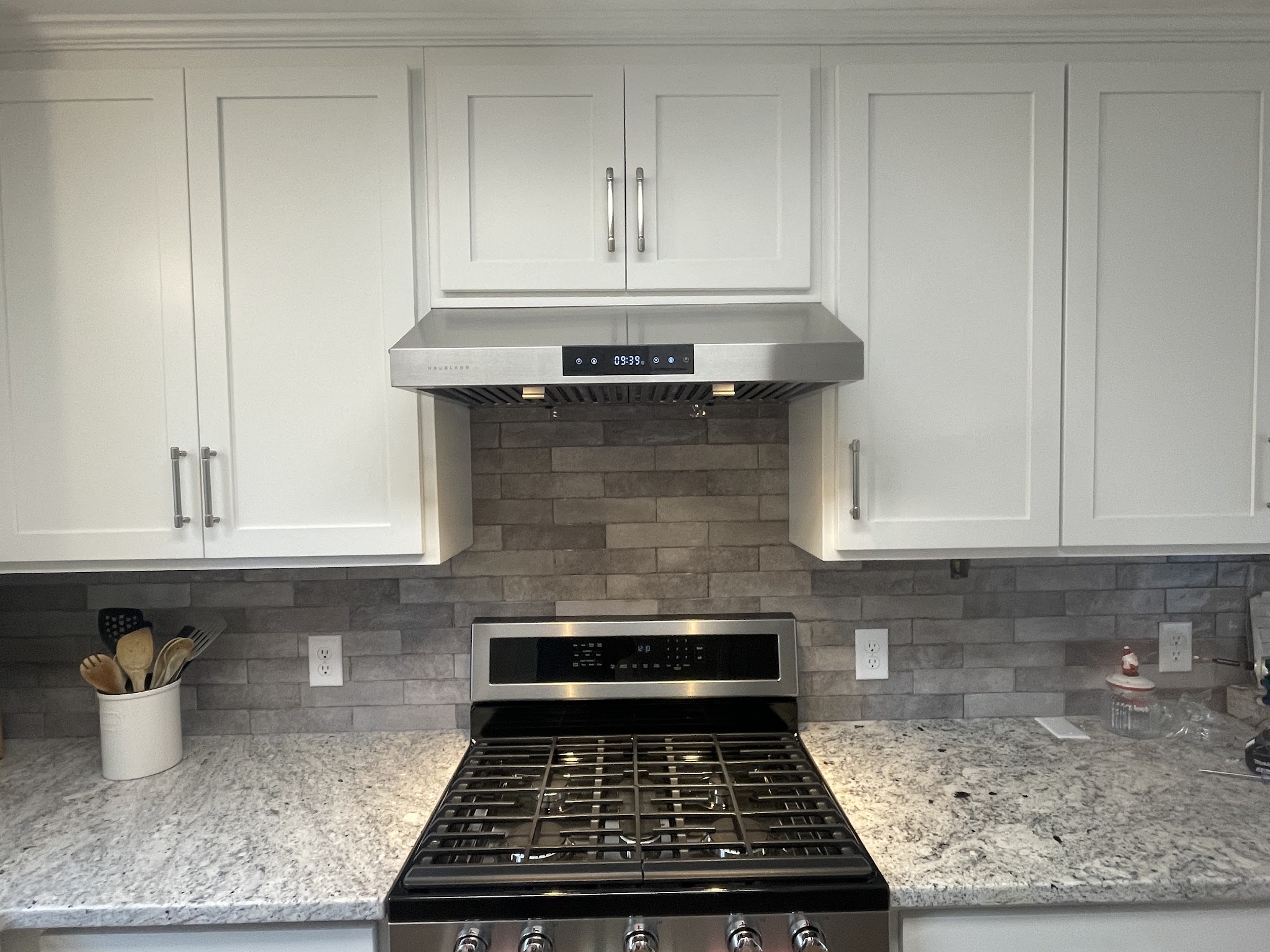 Finished kitchen with white cabinets, stone backsplash and range hood